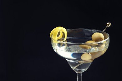 Photo of Martini cocktail with olives and lemon twist on dark background, closeup. Space for text