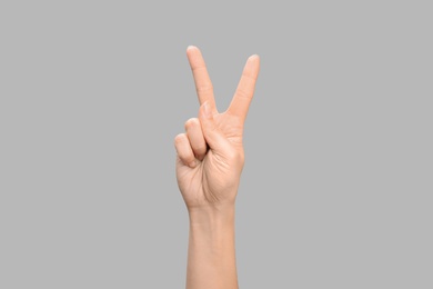 Photo of Woman showing V letter on grey background, closeup. Sign language