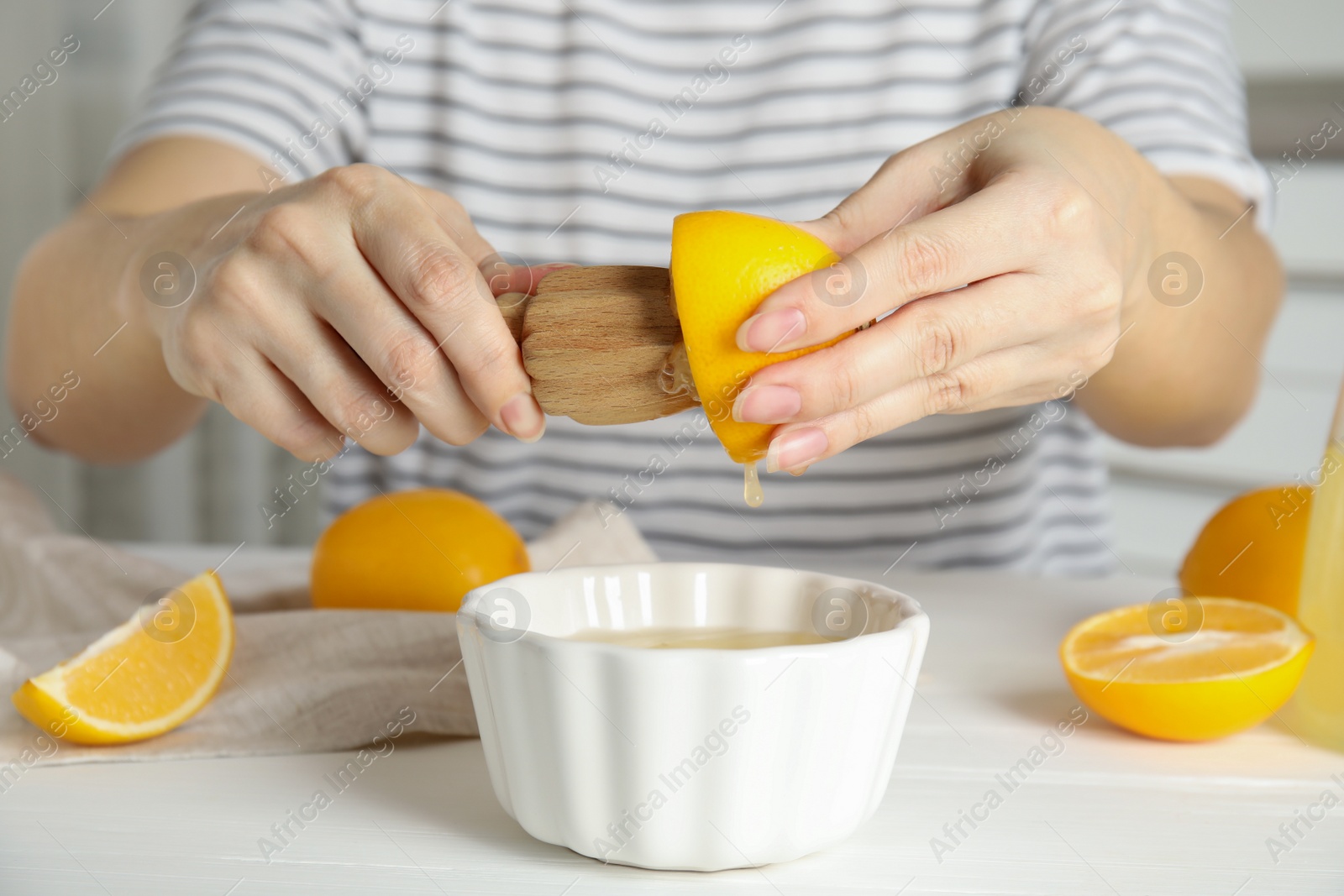 Photo of Woman squeezing lemon juice with wooden reamer at table, closeup