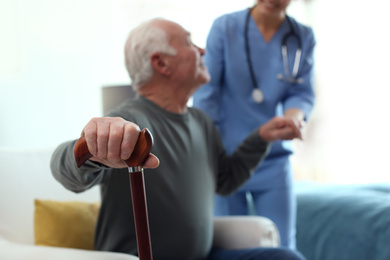 Photo of Care worker helping elderly man in geriatric hospice, focus on hand with stick