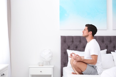 Man meditating on bed at home, space for text. Zen concept