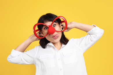 Photo of Funny woman with clown nose and large glasses on yellow background. April fool's day