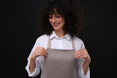 Happy woman wearing kitchen apron on black background. Mockup for design