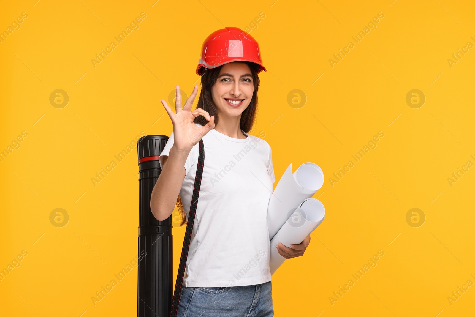 Photo of Architect in hard hat with drafts and tube showing ok gesture on yellow background