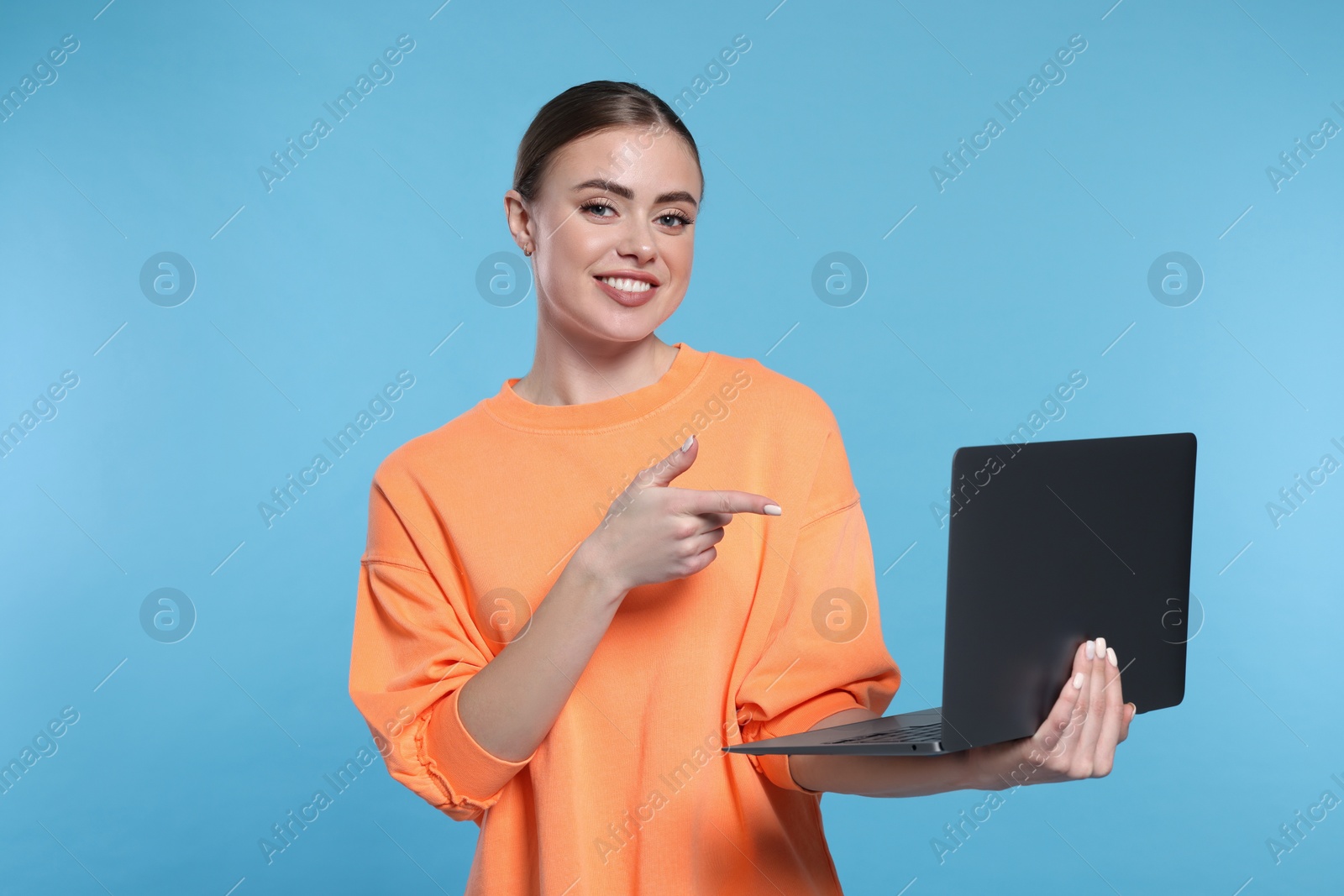 Photo of Happy woman pointing at laptop on light blue background