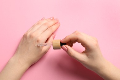 Photo of Woman dripping serum from pipette on her hand against pink background, closeup