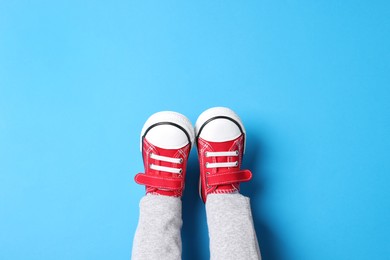 Little child in stylish red gumshoes on light blue background, top view