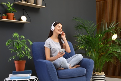 Happy woman listening to music in armchair at home. Indoor plants for trendy interior design