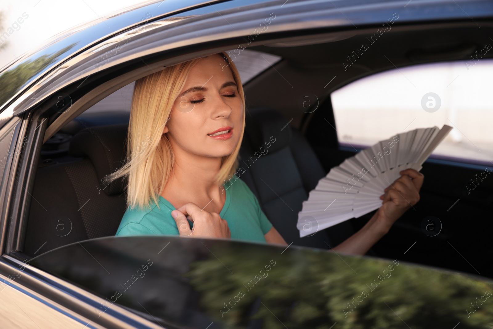 Photo of Woman with hand fan suffering from heat in car. Summer season