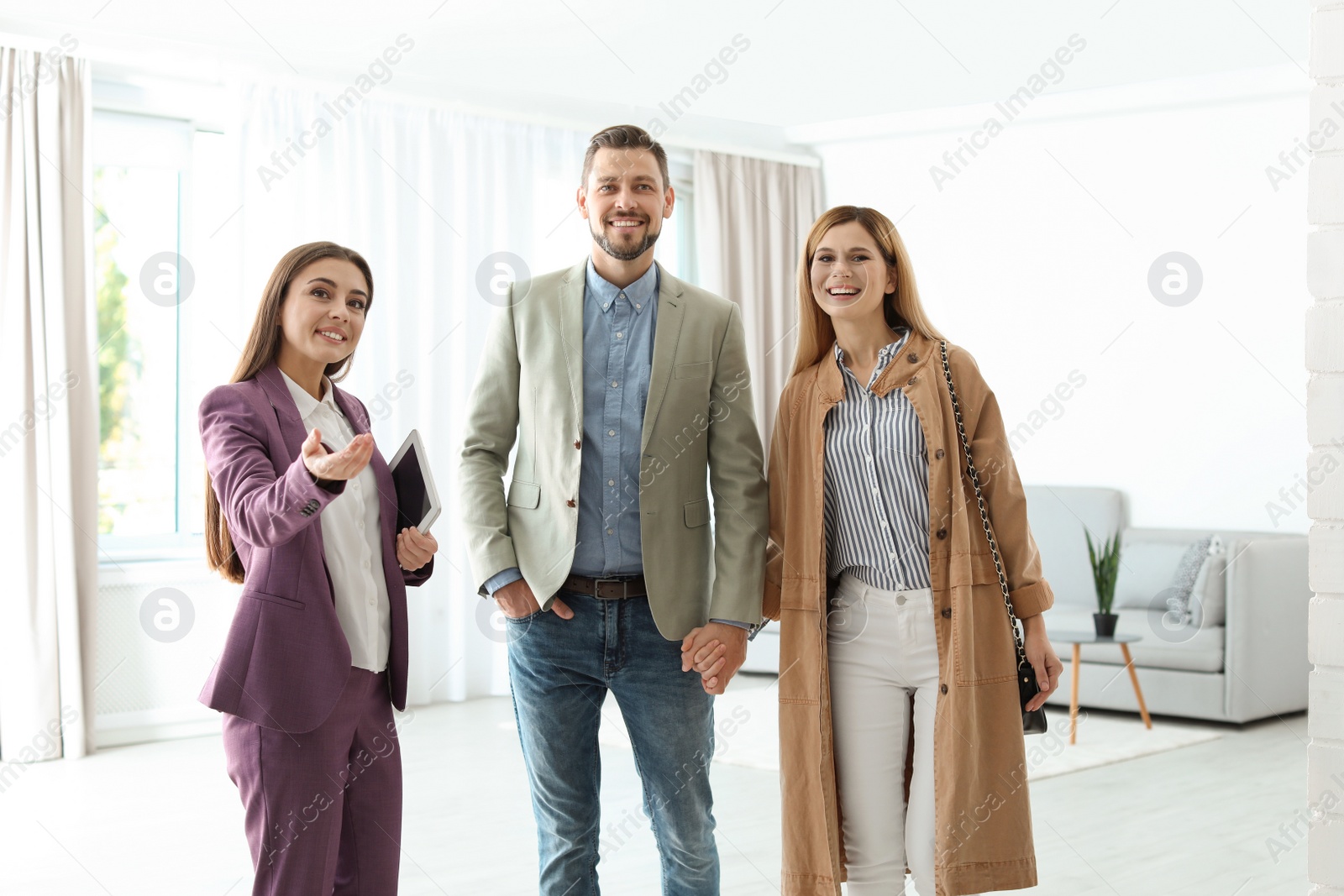 Photo of Female real estate agent showing new house to couple, indoors