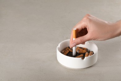 Photo of Woman putting out cigarette in ashtray on grey table, closeup. Space for text