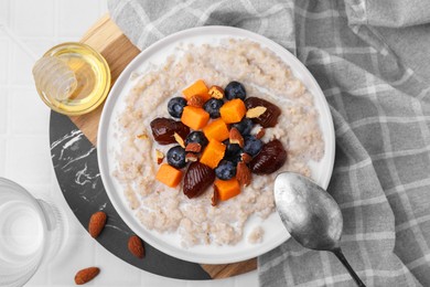 Photo of Delicious barley porridge with blueberries, pumpkin, dates and almonds served with honey on white table, flat lay