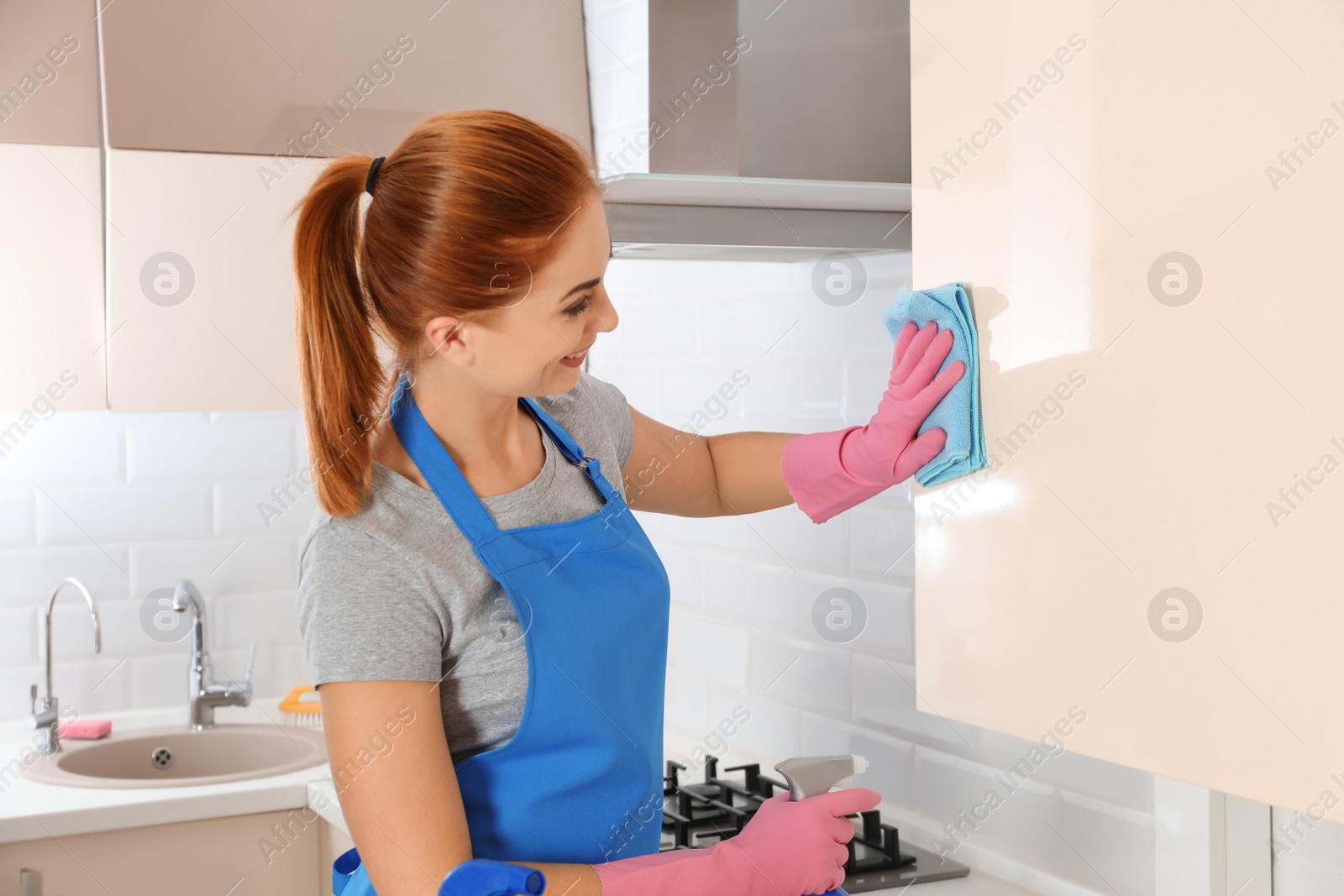 Photo of Woman in protective gloves cleaning kitchen with rag, indoors