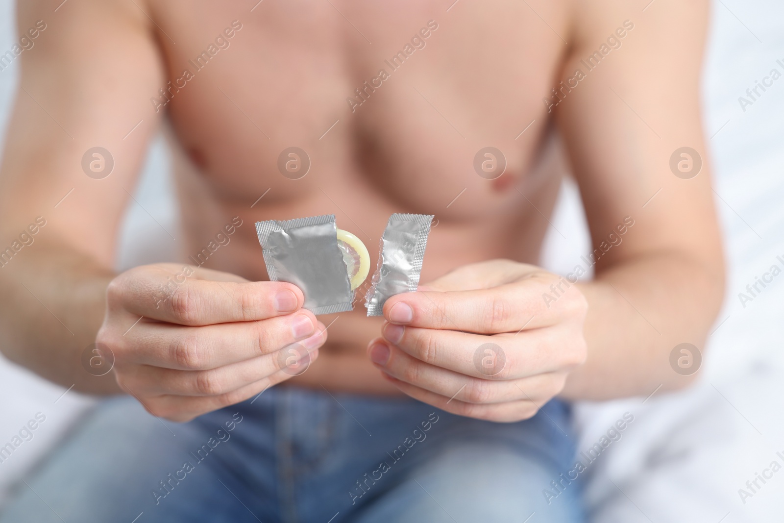 Photo of Closeup of man holding open pack with condom on bed