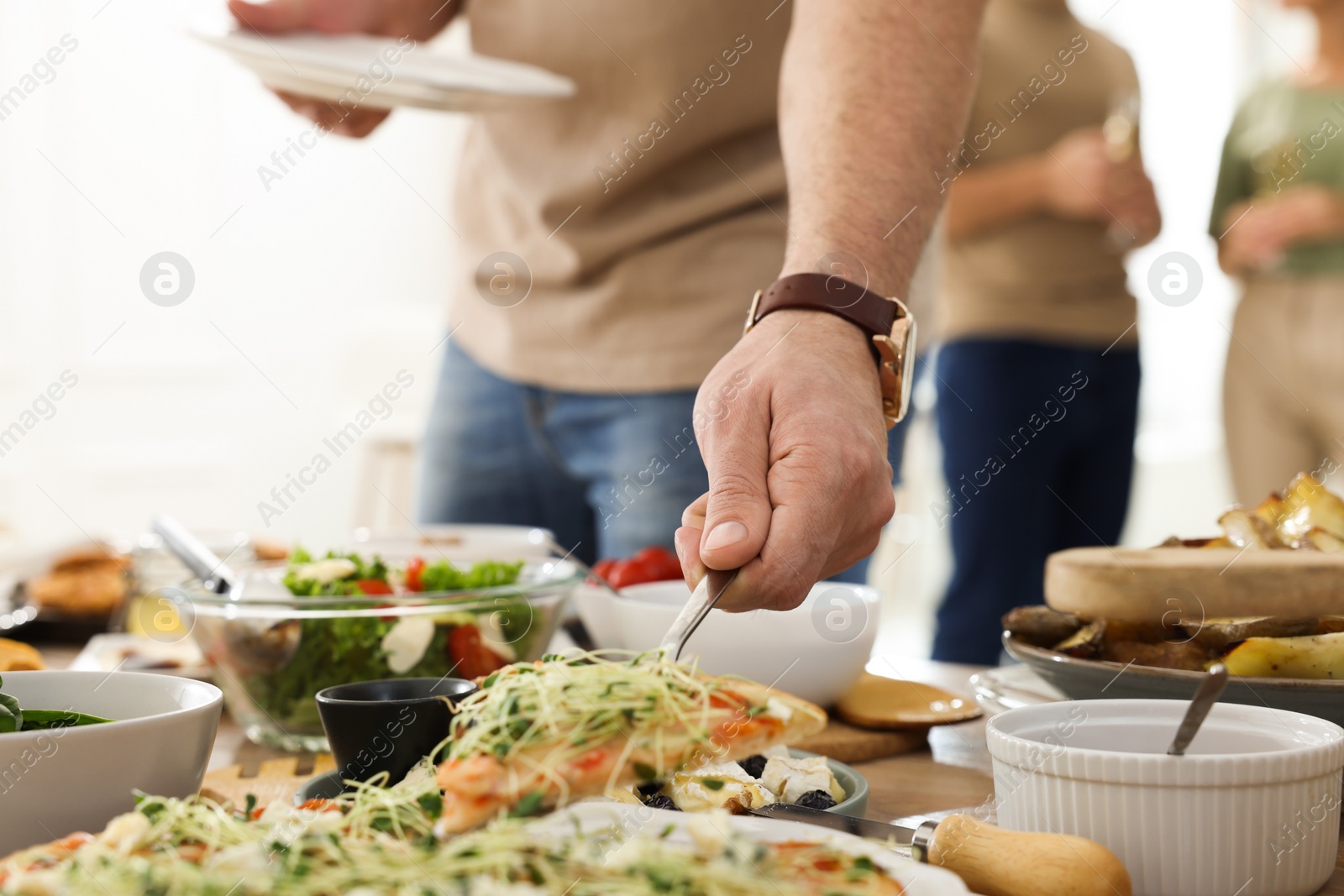 Photo of Man taking slice of pizza from buffet indoors, closeup. Brunch table setting