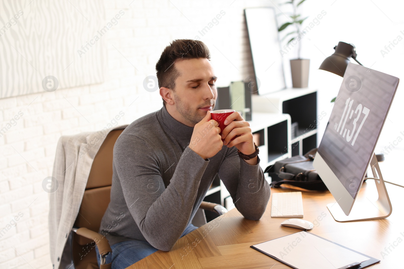 Photo of Young man with cup of drink relaxing at table in office during break