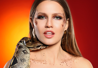 Photo of Beautiful woman with boa constrictor on bright colorful background, closeup