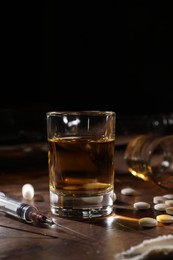 Photo of Alcohol and drug addiction. Whiskey in glass, syringe and pills on wooden table