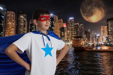 Image of Teenage boy wearing superhero costume and beautiful cityscape in night on background