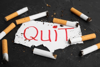 Cigarette stubs and paper with word Quit on black slate table. Giving up smoking concept