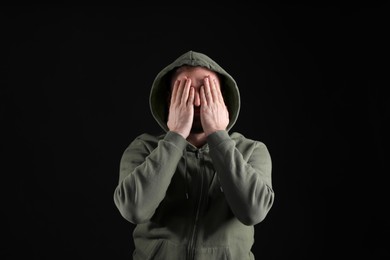 Young man covering face on black background. Personality concept