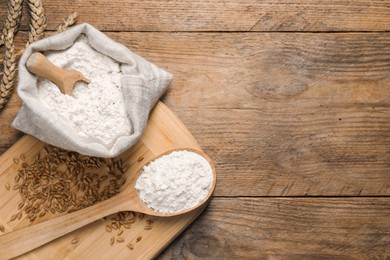 Photo of Wheat flour, grains and spikes on wooden table, flat lay. Space for text