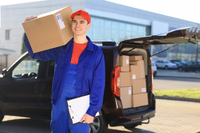 Photo of Courier with parcel and clipboard near delivery van outdoors