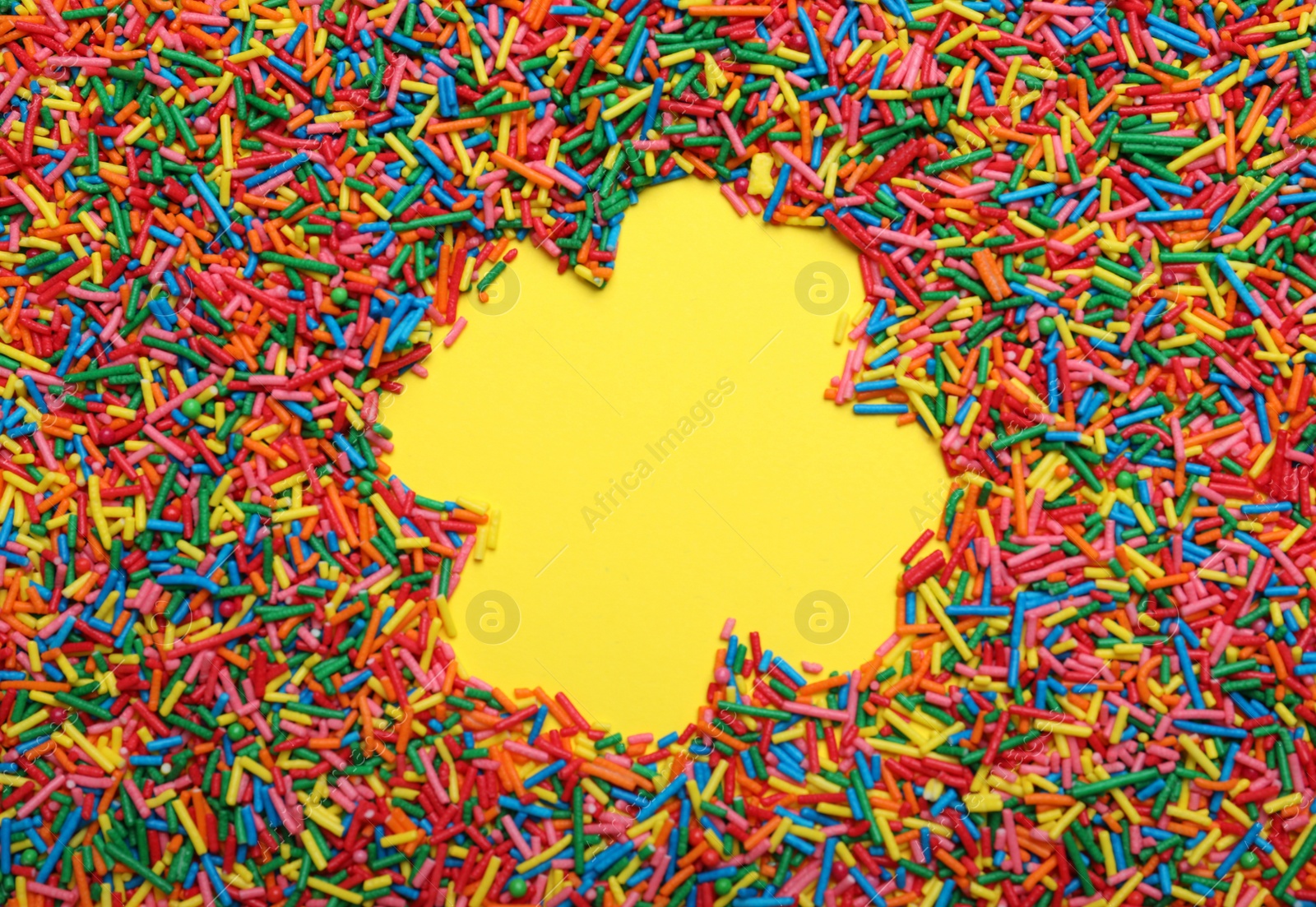 Photo of Clover shaped frame of sprinkles on yellow background, flat lay with space for text. Confectionery decor