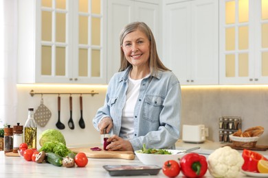 Photo of Happy woman cutting onion at table in kitchen