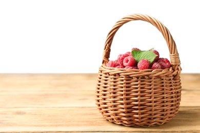 Photo of Basket of delicious fresh ripe raspberries with leaves on wooden table against white background, space for text