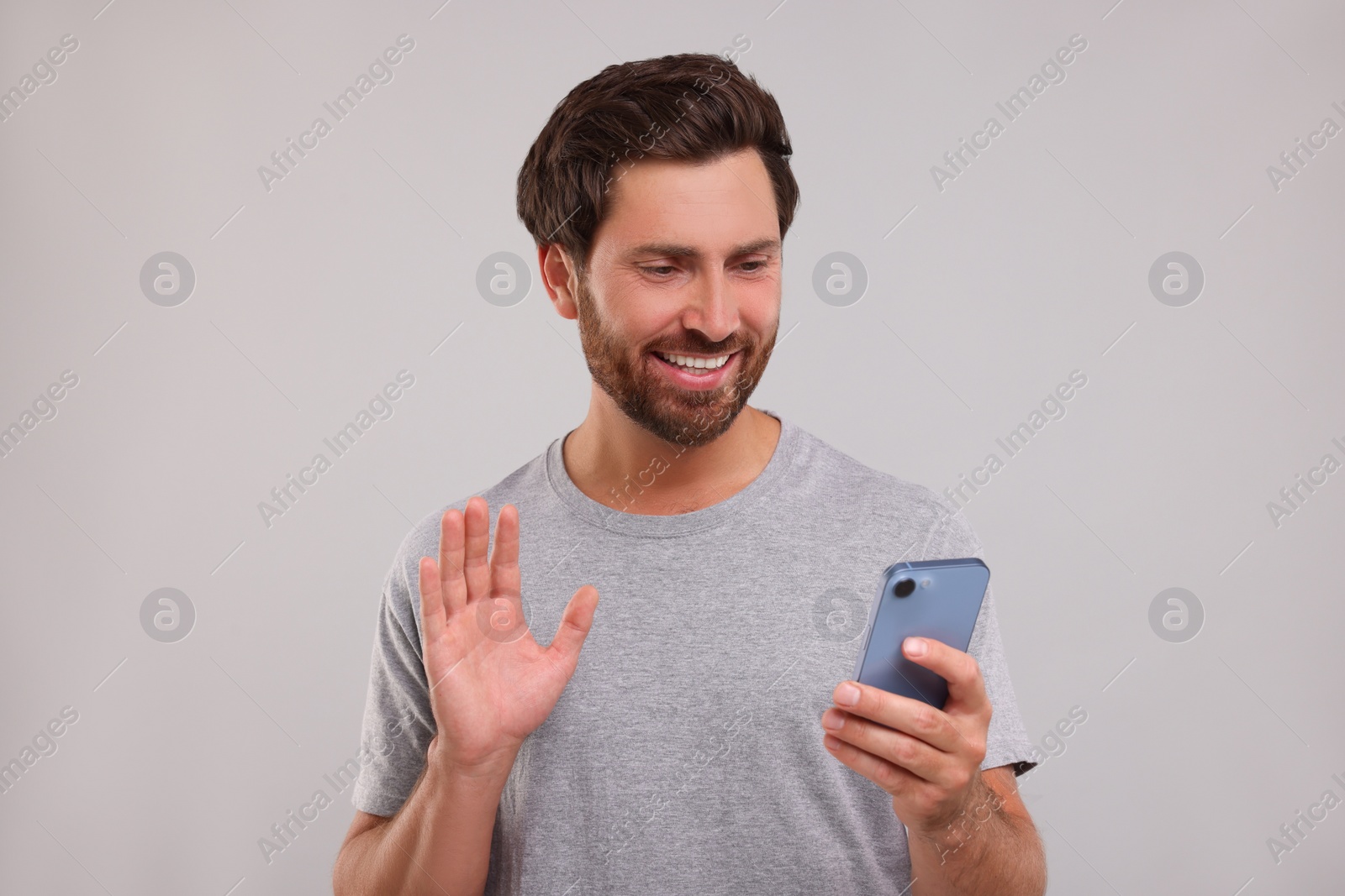 Photo of Handsome bearded man using smartphone on grey background