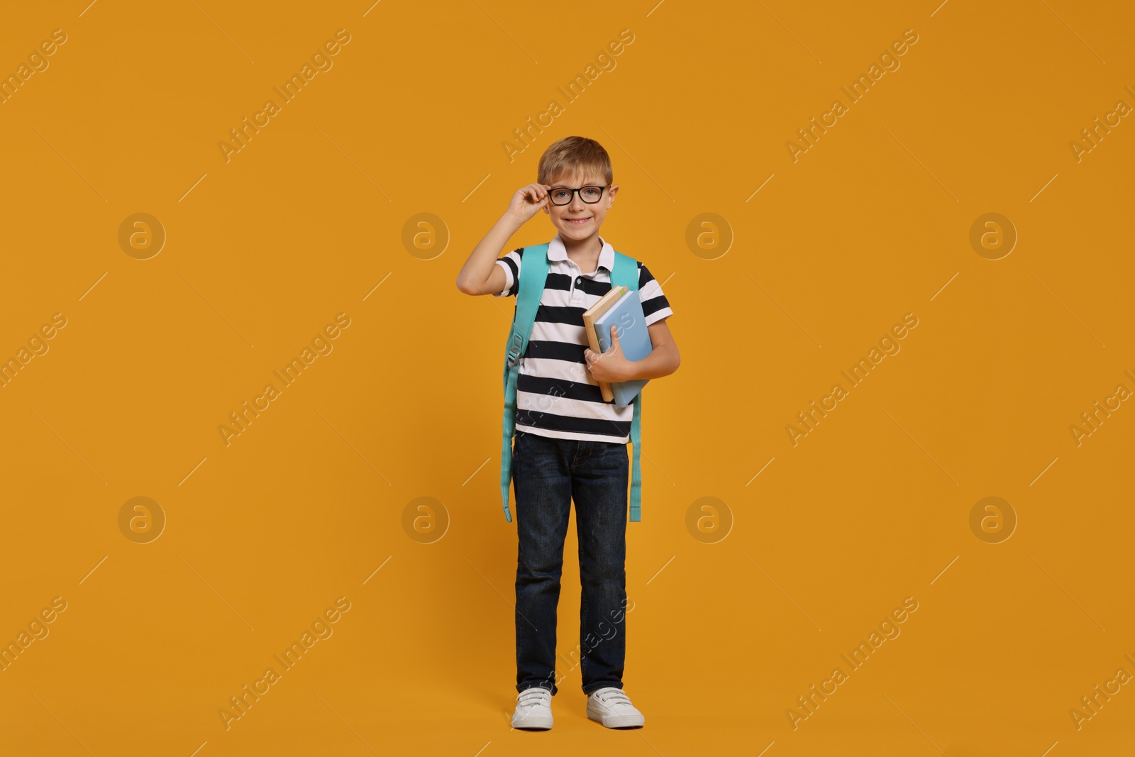 Photo of Happy schoolboy in glasses with backpack and books on orange background