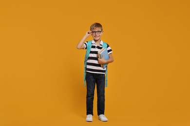 Photo of Happy schoolboy in glasses with backpack and books on orange background