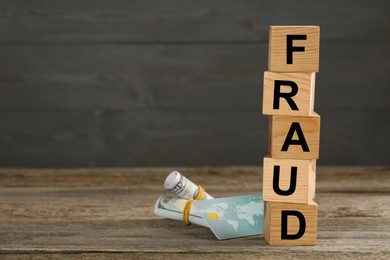 Photo of Cubes with word Fraud, credit card and money on wooden table, space for text