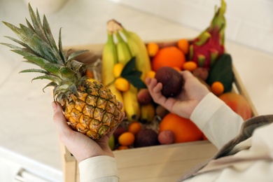 Woman with assortment of exotic fruits at table in kitchen, closeup