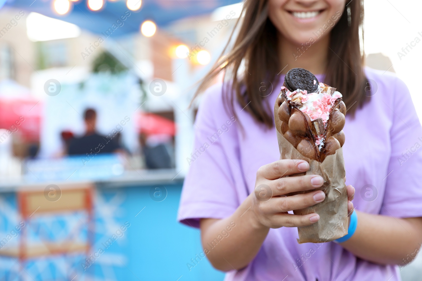 Photo of Young woman holding delicious sweet bubble waffle with ice cream outdoors, closeup