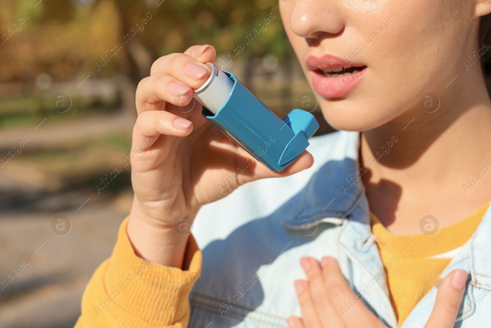 Photo of Woman using asthma inhaler outdoors. Health care