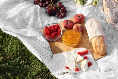 Photo of Picnic blanket with tasty food, flowers and basket on green grass outdoors