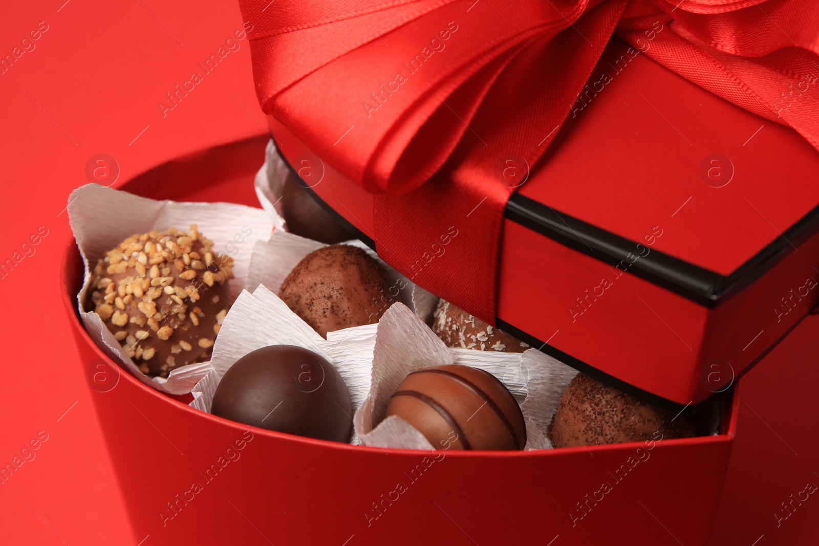 Photo of Heart shaped box with delicious chocolate candies on red table, closeup