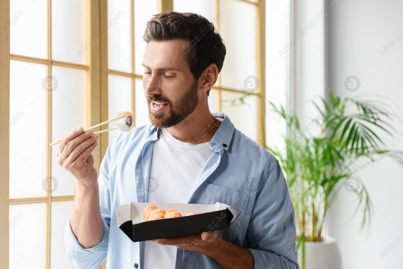 Photo of Handsome man eating sushi rolls with chopsticks indoors