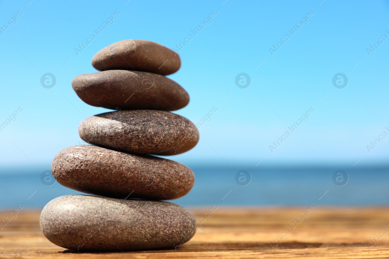 Photo of Stack of stones on wooden table against seascape, space for text. Zen concept