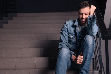 Upset man sitting on stairs indoors, space for text. Loneliness concept