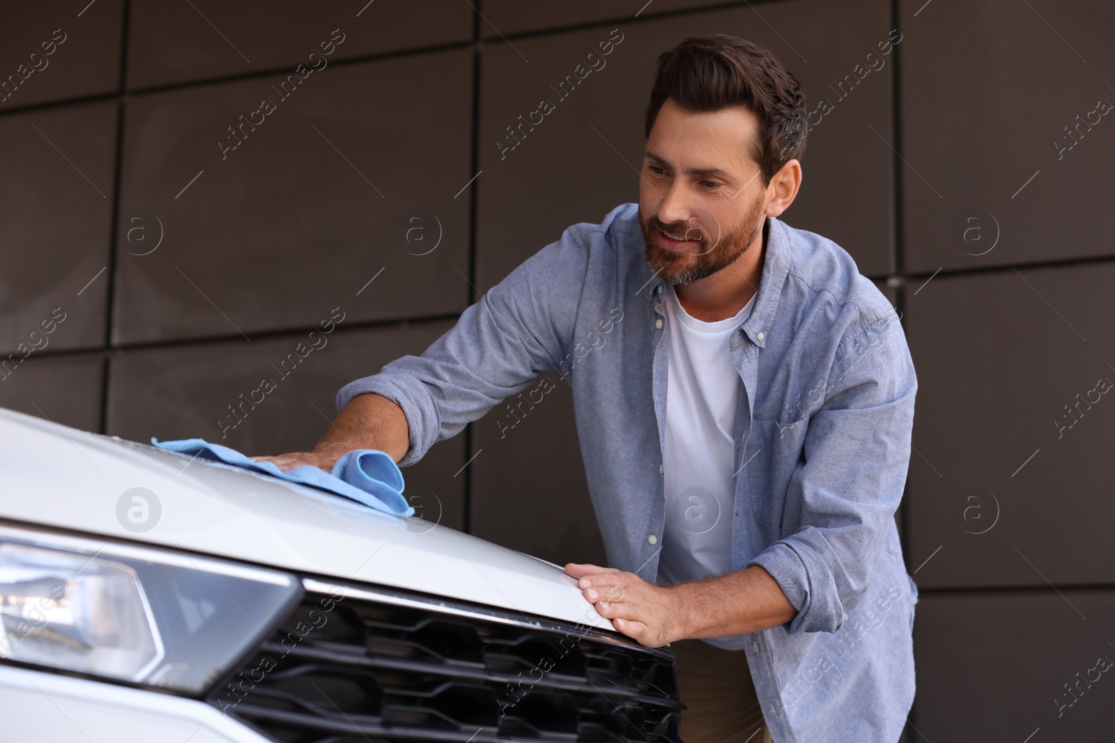 Photo of Handsome man cleaning car hood with rag outdoors