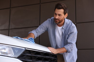 Photo of Handsome man cleaning car hood with rag outdoors
