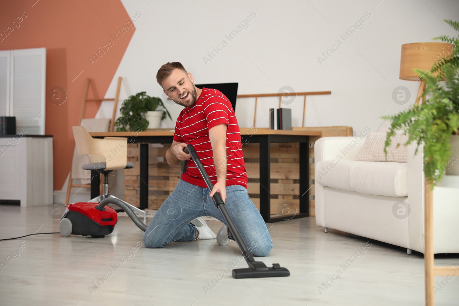 Photo of Young man having fun while vacuuming at home