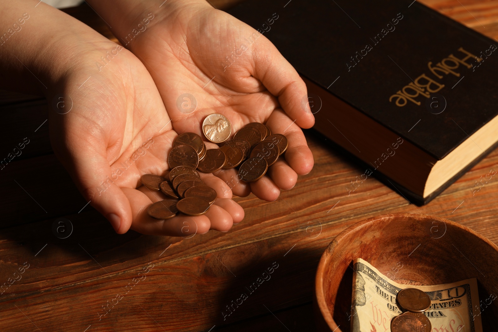 Photo of Donate and give concept. Woman holding coins, closeup. Bible and bowl of money on wooden table