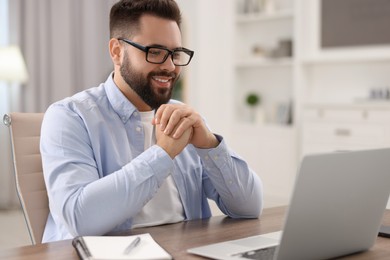 Photo of Young man in glasses watching webinar at table in room