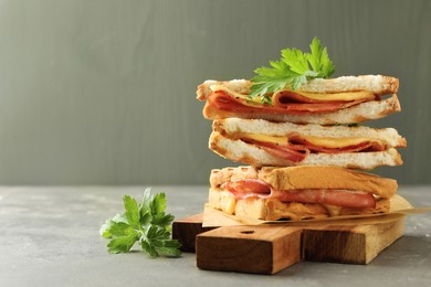 Photo of Stack of tasty sandwiches with ham, parsley and melted cheese on grey table. Space for text