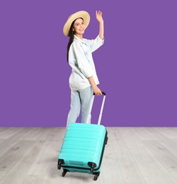 Photo of Beautiful woman with suitcase for summer trip near purple wall. Vacation travel