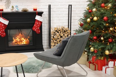 Beautiful Christmas tree near fireplace and cosy armchair in room. Interior design